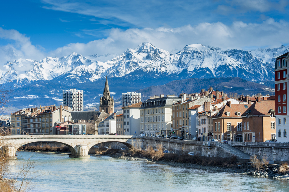 een brug, de rivier en gebouwen in Grenoble, met op de achtergrond bergen met besneeuwde toppen