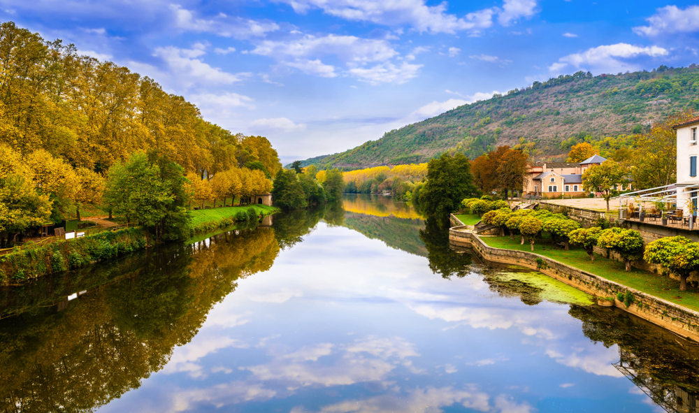 foto van de rivier de Aveyron in de herfst met aan de zijkant bruin gekleurde bomen die in het water weerspiegelen samen met de blauwe lucht en witte wolken