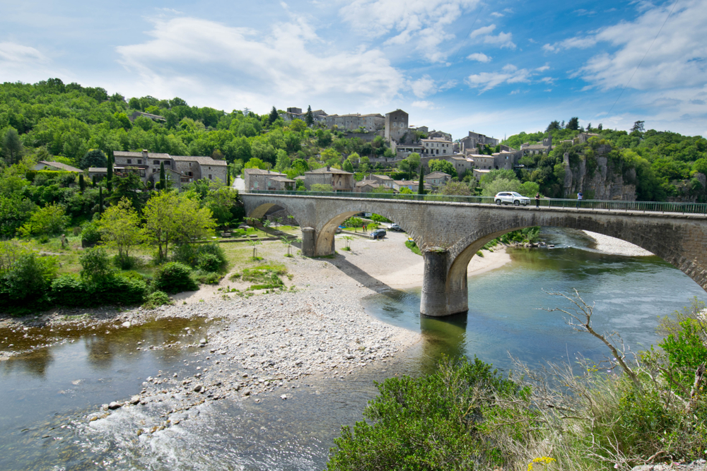 stenen boogbrug over een rivier en op de achtergrond het dorpje Balazuc in de Ardèche