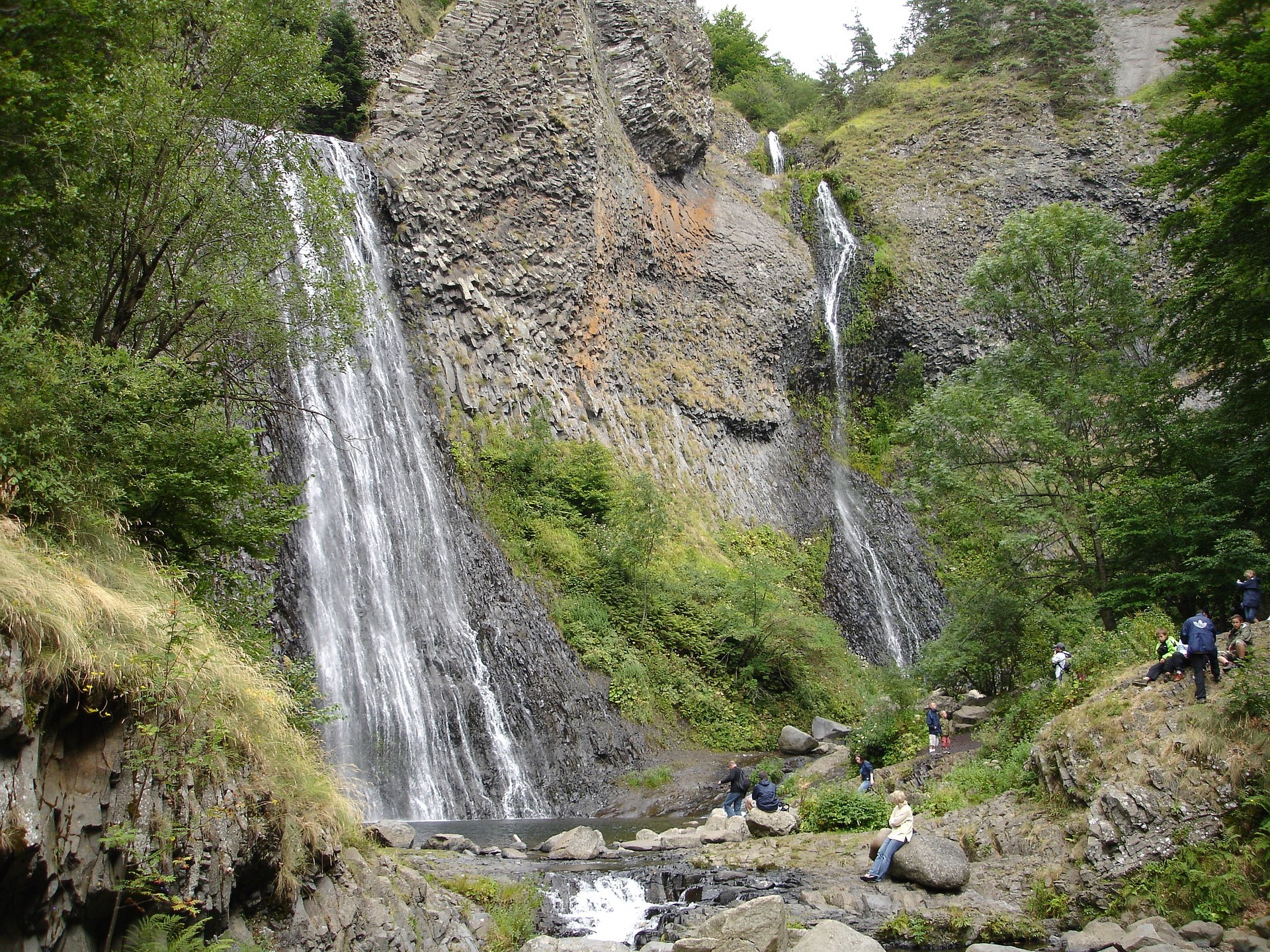 twee watervallen die steil naar beneden kletteren met beneden rotsen en mensen gekleed in regenkleding bij de Cascade du Ray-Pic in de Ardèche