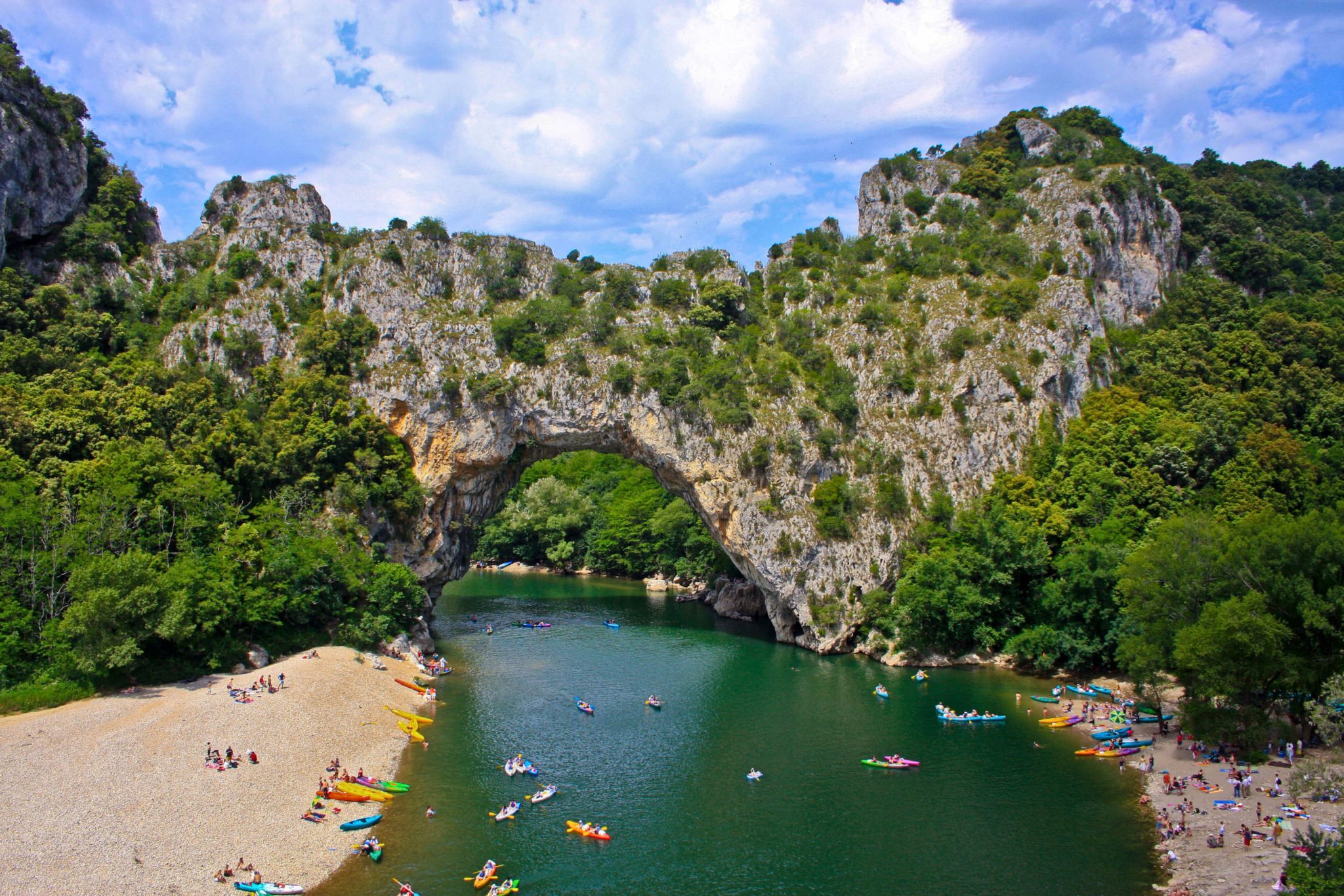 de Pont d’Arc, een natuurlijke boog over het water in de Ardèche, met aan beide kanten van de rivier strandjes met mensen en kano's in allerlei kleuren