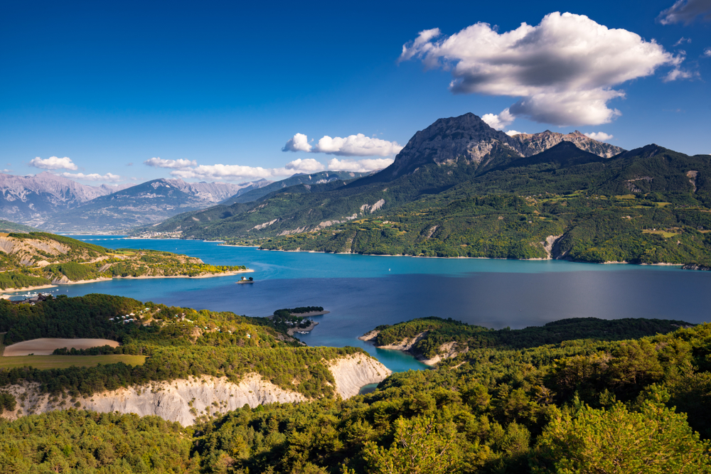 Lac de Serre-Ponçon helderblauw meer omgeven door bergen en groene vegetatie