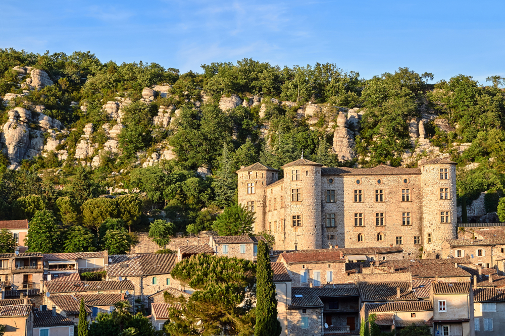 stenen huizen met daar achter een groot kasteel en een begroeide rotswand in het stadje Vogüé in de Ardèche