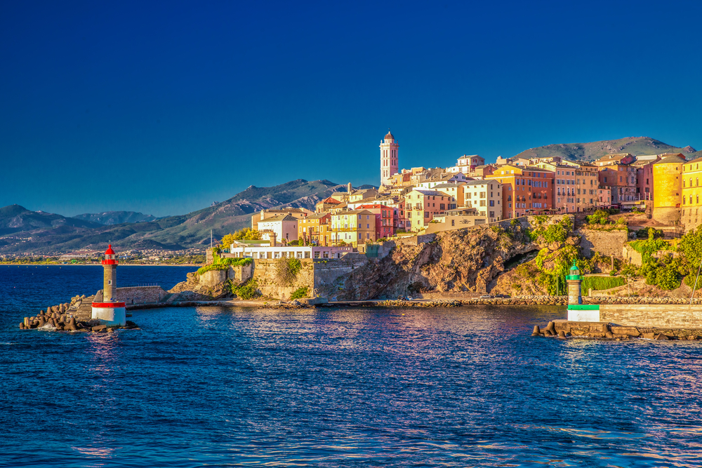 gekleurde huisjes en een kerktoren op een rots aan zee tijdens het gouden uur in Bastia, Corsica 