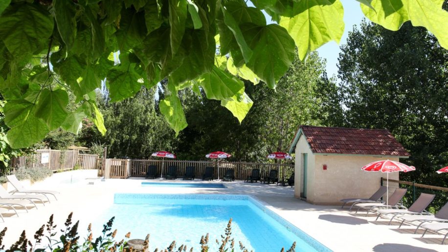 leeg, omheind zwembad met aan de rand zonnebedjes en ola parasols op Camping L'Offrerie in de Dordogne