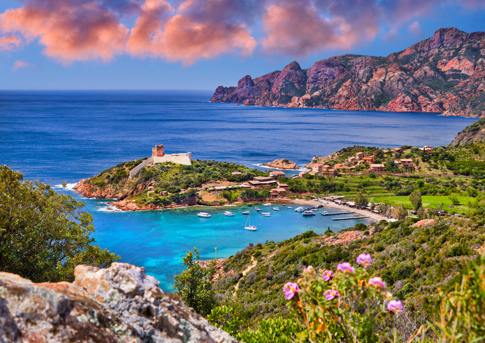 bootjes in een azuurblauwe baai, omringd door een groene omgeving met bergen en planen in het Reserva Natural de Scondaola op Corsica