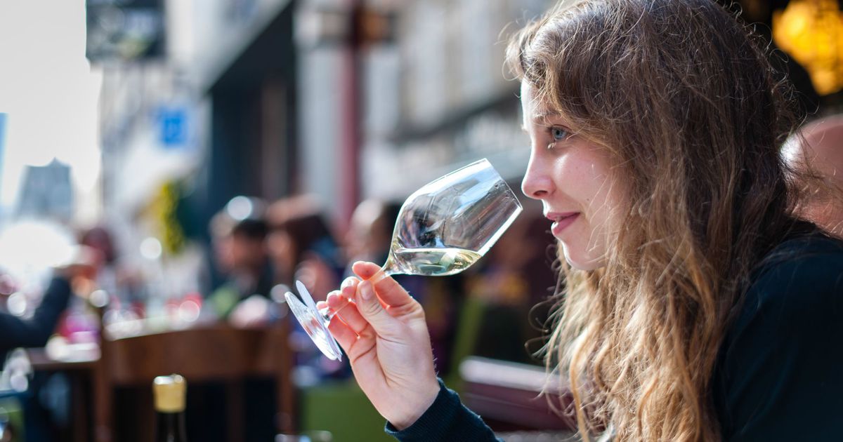 jonge vrouw met een glas witte wijn in haar hand die zij naar mond toe brengt