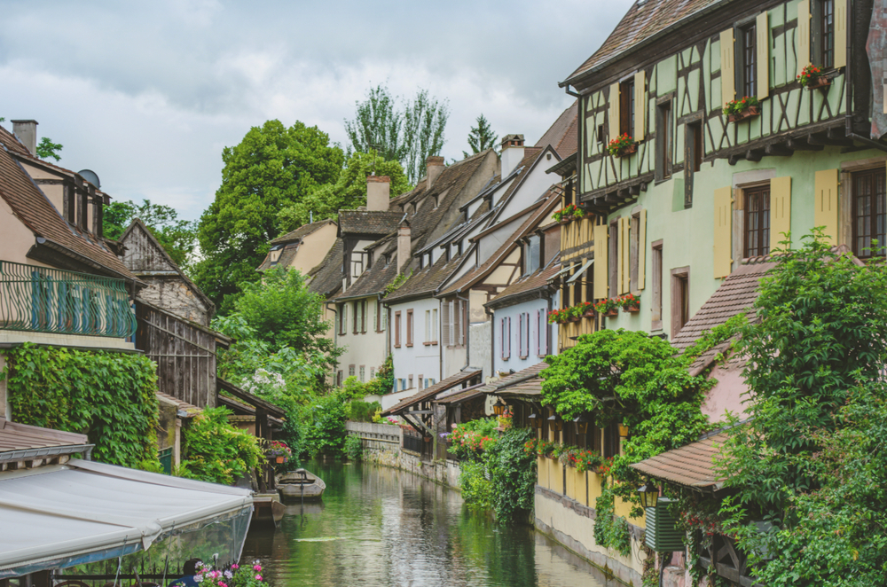 kanaaltje met een leeg bootje, gekleurde huizen en aan de zijkanten struiken in Mulhouse op een bewolkte dag