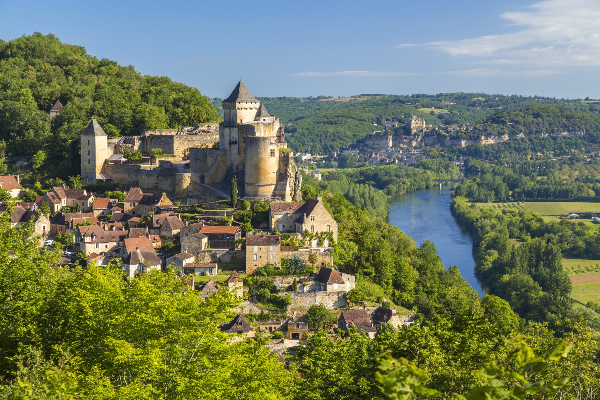 kasteel dat boven een dorpje uittorent gelegen op een heuvel in de Dordogne. Beneden in het dal stroomt de rivier.