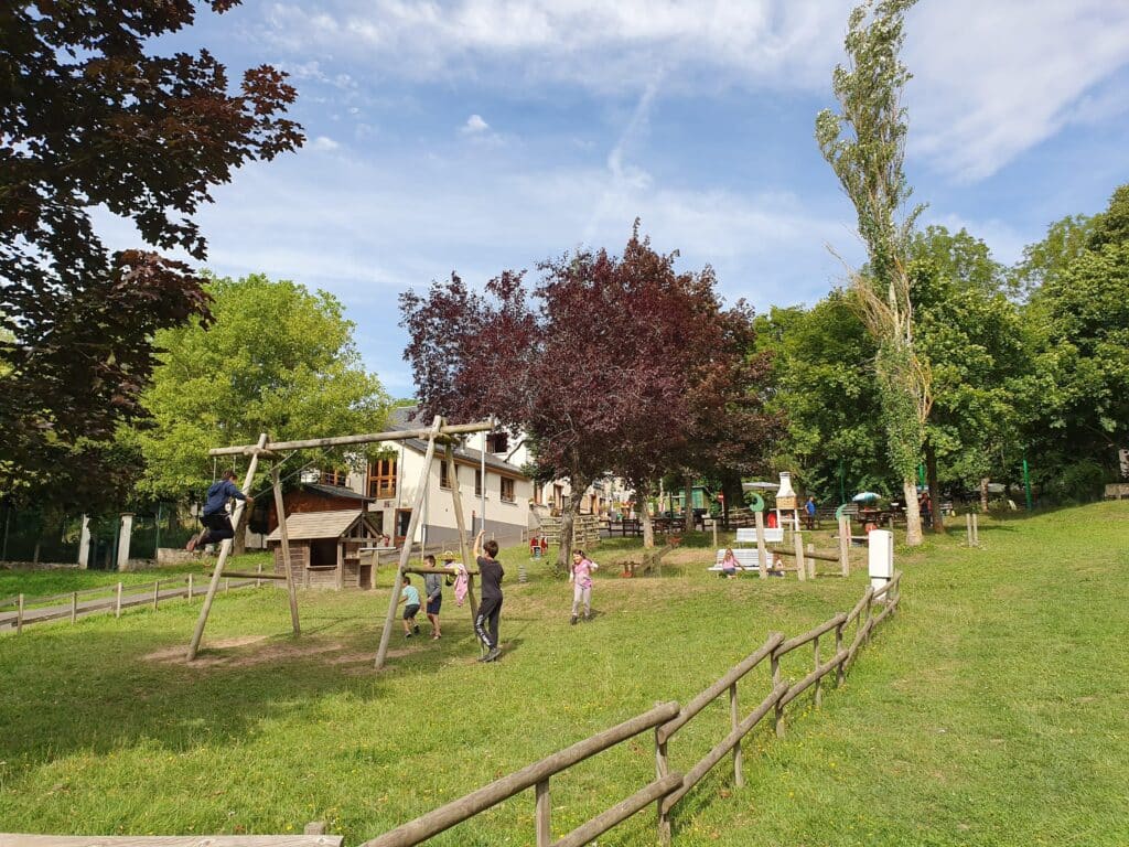 kinderen in een speeltuin met schommel, huisje, wipwap en nog enkele speeltoestellen in het gras op Camping de la Haute Sioule