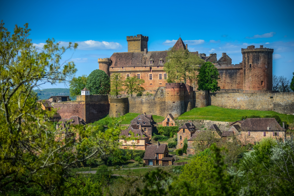 Het Middeleeuwse kasteel Château de Castelnau-Bretenoux op een zonnige dag met daarvoor kleine, middeleeuwse huisjes.
