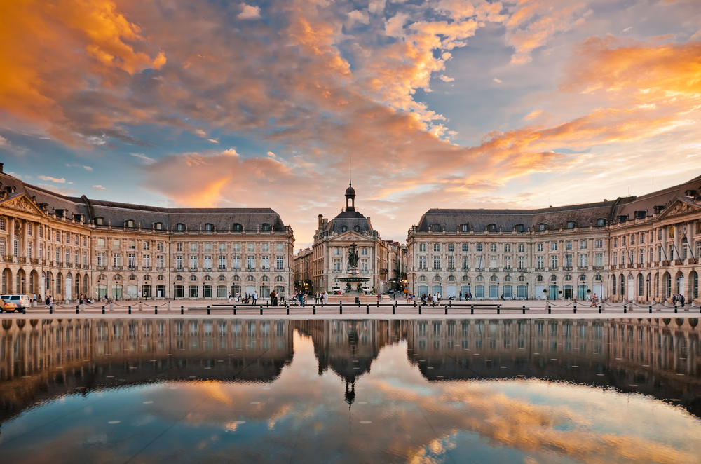 Place de la Bourse tijdens zonsondergang in Bordeaux. Het paleis en de roze wolken weerspiegelen in het water van de weide fontein