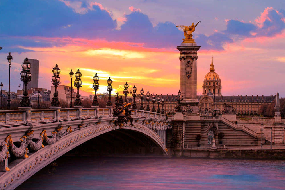 foto van een brug in Parijs over de Seine met op de achtergrond een mooi groot gebouw en een paarse lucht