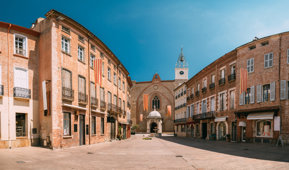 pleintje met rondom huizen en een aan het einde een kerk op een strakblauwe dag in Perpignan