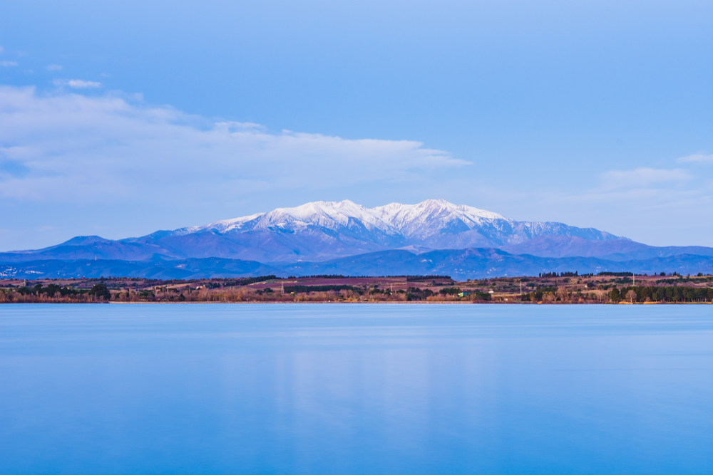 het Massif du Canigou gezien vanaf het water. Hoog op de bergen ligt sneeuw.