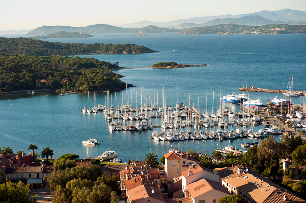 de kleine haven van Île de Porquerolles. De haven ligt vol met bootjes, maar straalt kalmte uit. Op de achtergrond zie je andere eilandjes en bergen liggen.