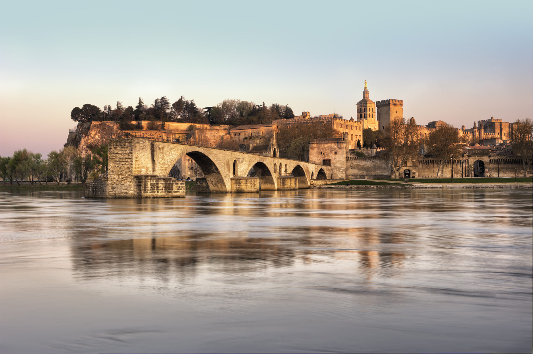 foto van 4 bogen van een brug in de rivier de Rhône, de brug stopt midden in het water en op de achtergrond ligt een historisch stadje met oude torens en stadsmuren
