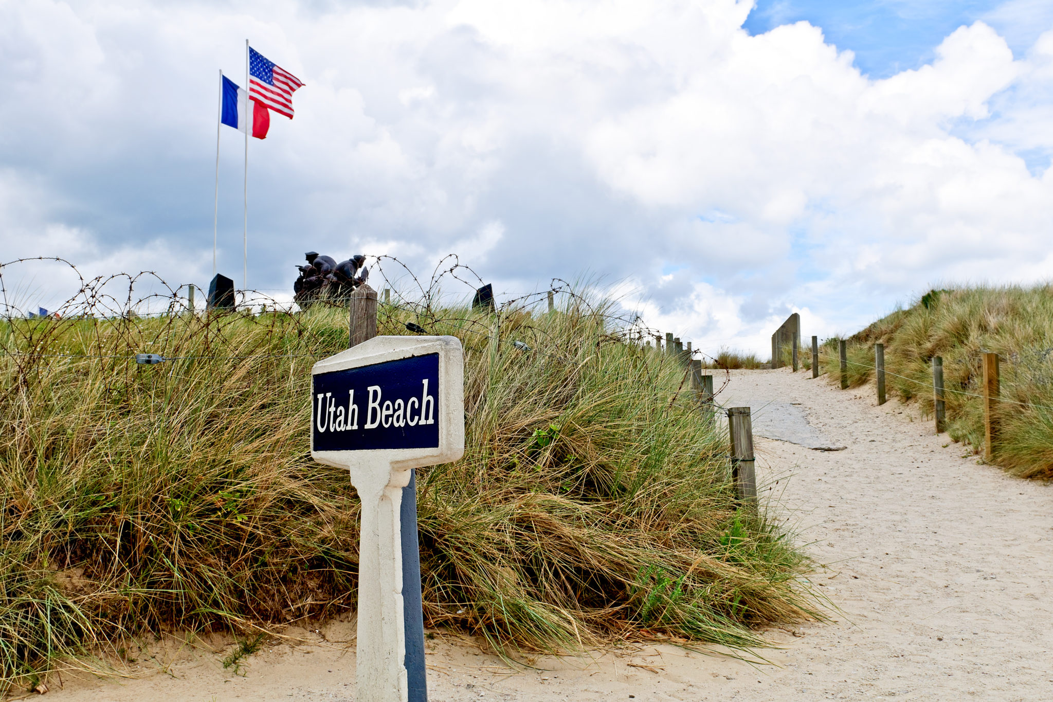 toegang tot het landingsstrand Utah Beach met naast het pad een bordje waarop in het wit met zwarte achtergrond staat 'Utah Beach'