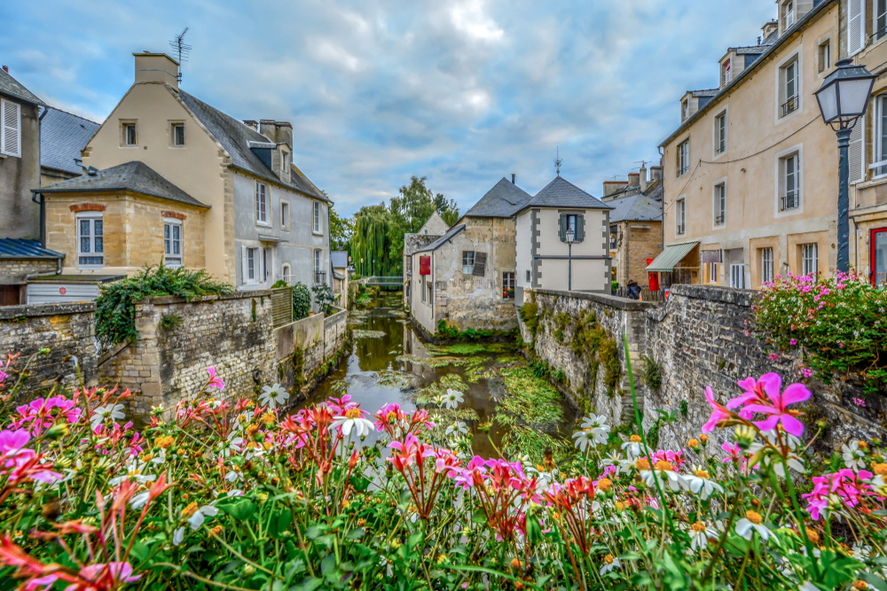 Rivier in Bayeux met vakwerkhuizen aan het water en kleurrijke bloemen.
