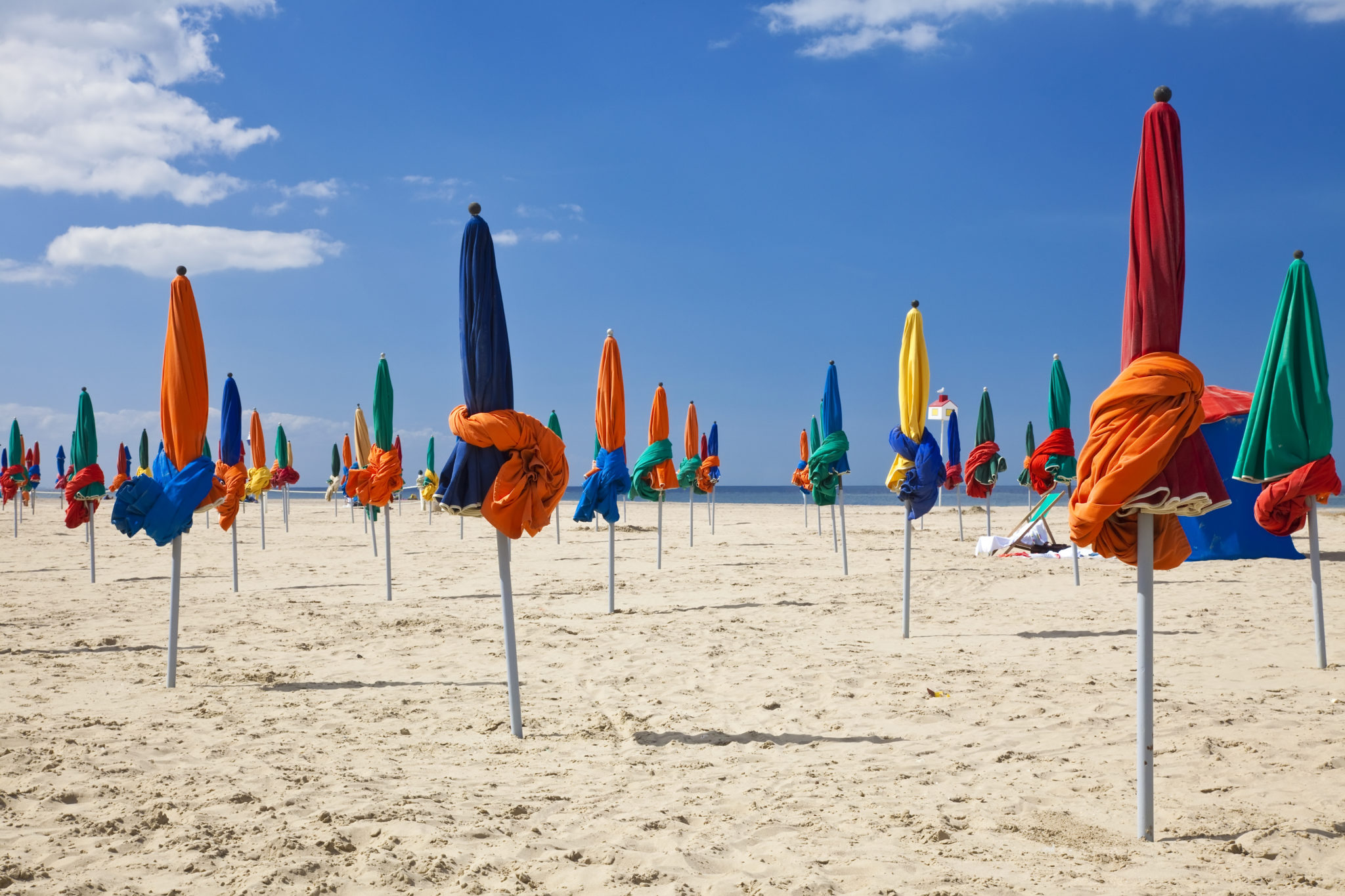 gekleurde, dichte parasollen op het strand van Deauville op een zonnige dag. Er zijn geen mensen op het strand en de parasollen hebben de kleuren groen, geel, oranje, rood en blauw.