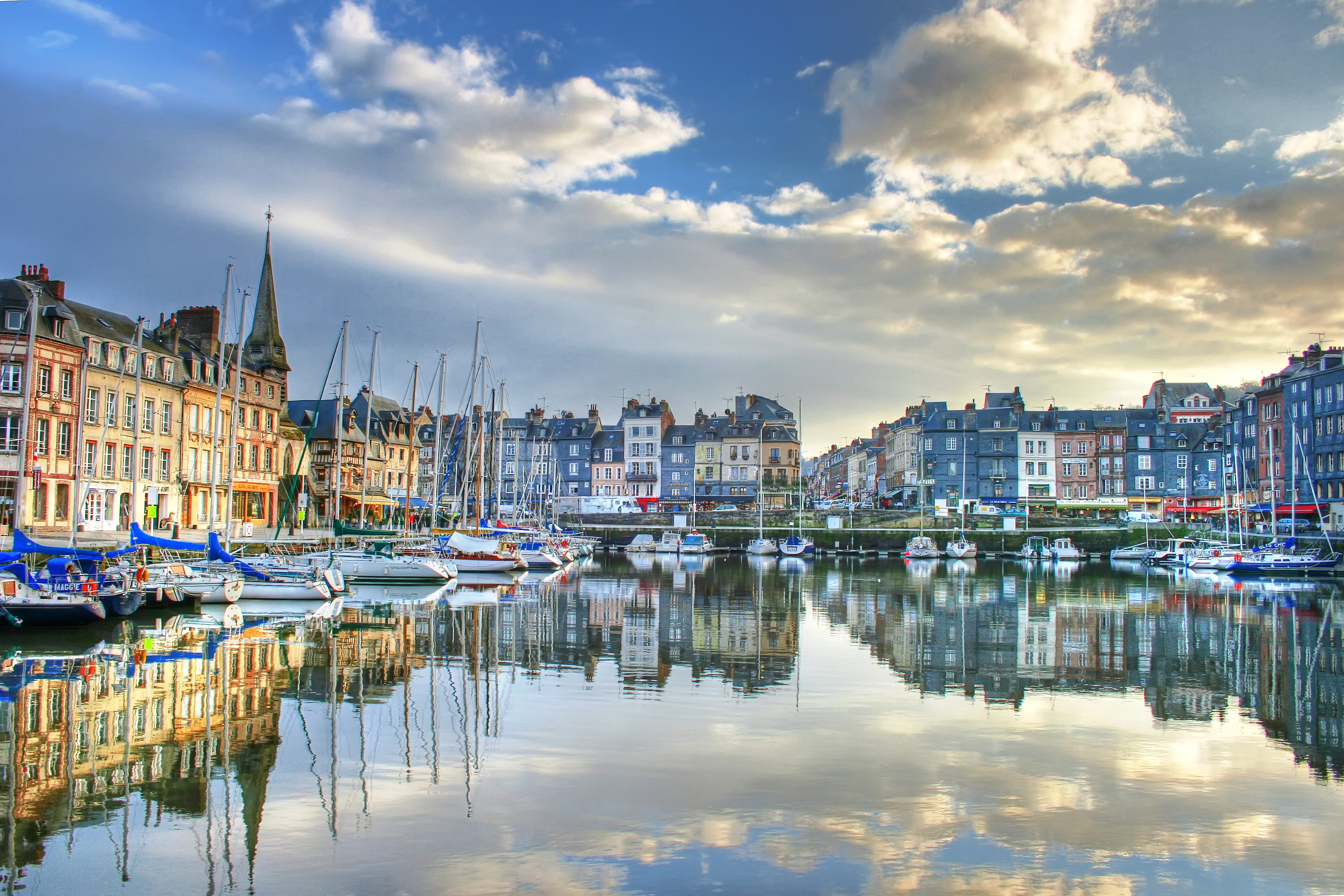 De haven van Honfleur met vissersbootjes in het water en omringd door pittoreske vakwerkhuizen.