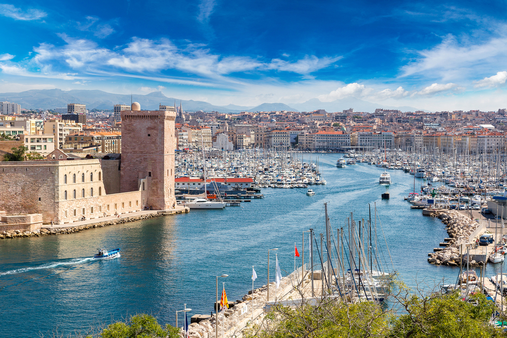 de grote haven van Marseille waar honderden boten liggen. Aan de linkerkant ligt een oud fort en achter de haven zie je de stad liggen 