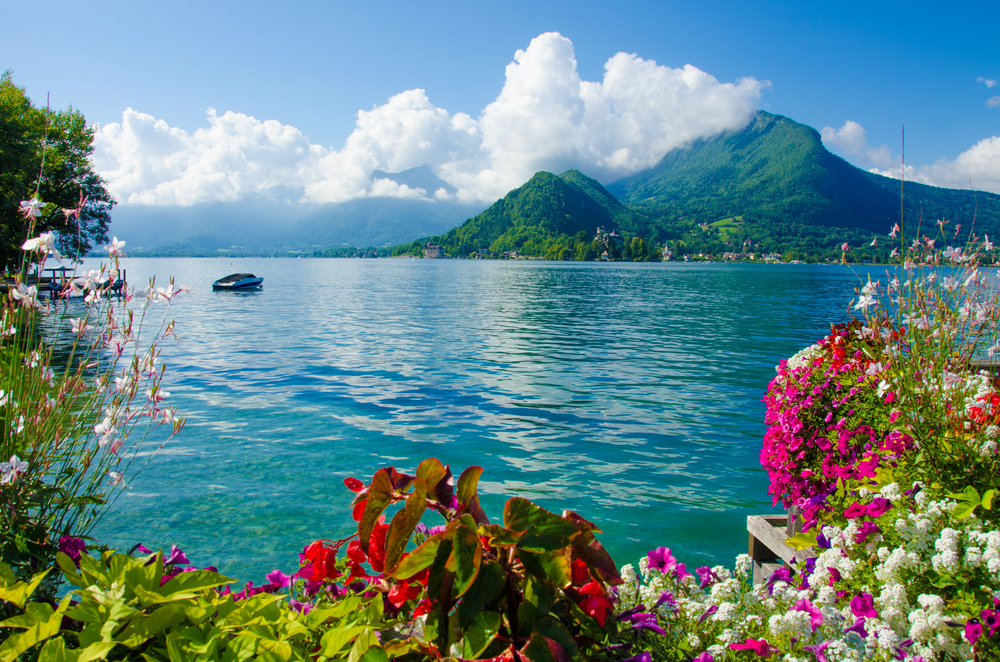 Het blauwe meer van Annecy omringd door groene bergen en kleurrijke bloemen.