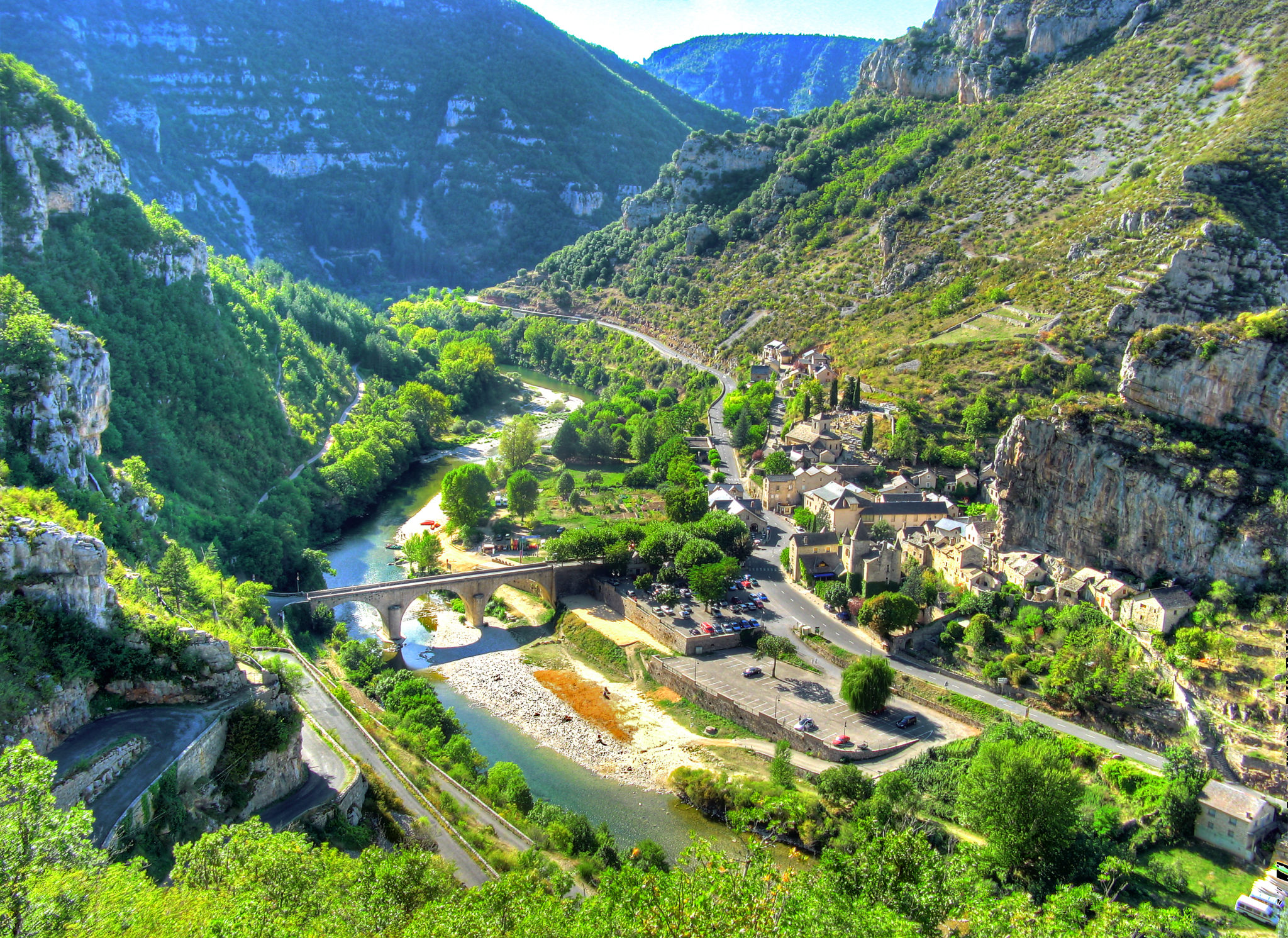 foto van de Gorges du Tarn. In het dal stroomt een rivier die bijna droog ligt en aan de kant zijn parkeerplaatsen en een oud dorpje