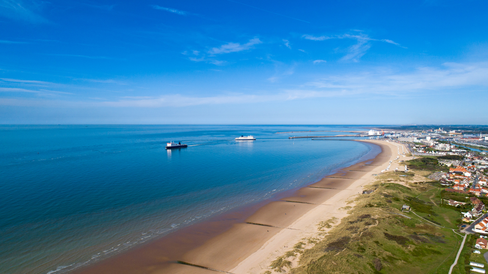 dus kust bij het plaatsje Calais met het strand, twee boten op het water en de duinen met daarachter de huizen