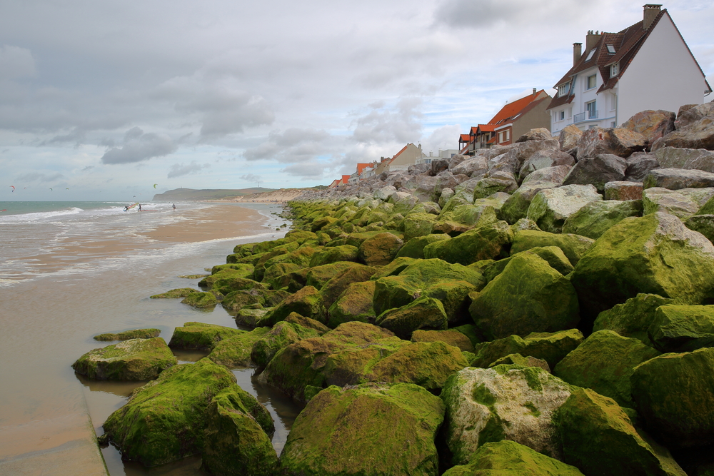 strand met aan de rechterkant keien en huizen op de dijk in Wissant op een bewolkte dag