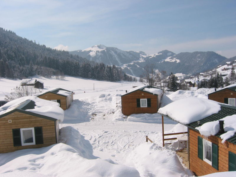 vijf houten chalets gelegen tussen een dik pak sneeuw op Camping Capfun Le Plan du Fernuy in de Franse Alpen