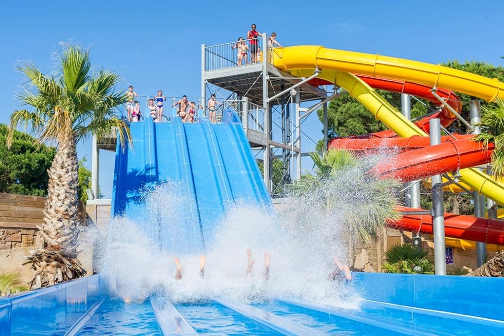 mensen die van een vierdubbele glijbaan afroetsjen en bovenaan kinderen en aan de zijkant nog drie andere glijbanen