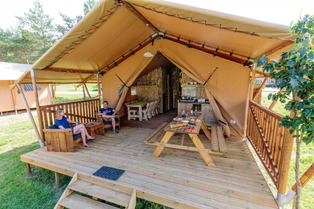 een man en een vrouw die op de loungestoelen op het overdekte terras van hun safaritent zitten