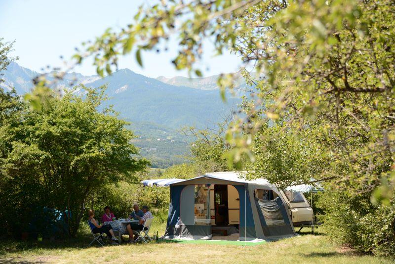 caravan met een voortent op Camping Sites et Paysages Le Petit Liou. Naast de voortent zitten twee mannen en twee vrouwen aan een tafel in de schaduw.