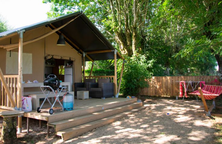 Safaritent die open is met een terras met loungestoelen, picknicktafel en bankjes, een barbecue en iets voor de tent een hangmat en droogrek