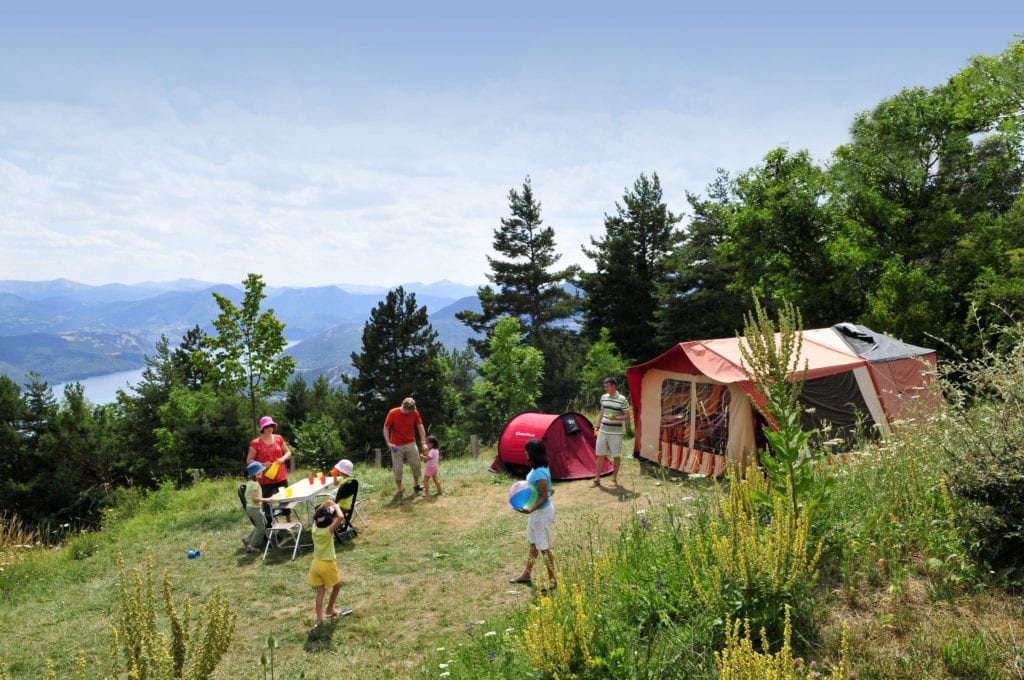 uitzicht vanaf camping Campéole Le Clos du Lac met op de achtergrond beneden het meer en op de voorgrond ee kampeerplaats met twee tenten en mensen die op het veld rondlopen en spelen