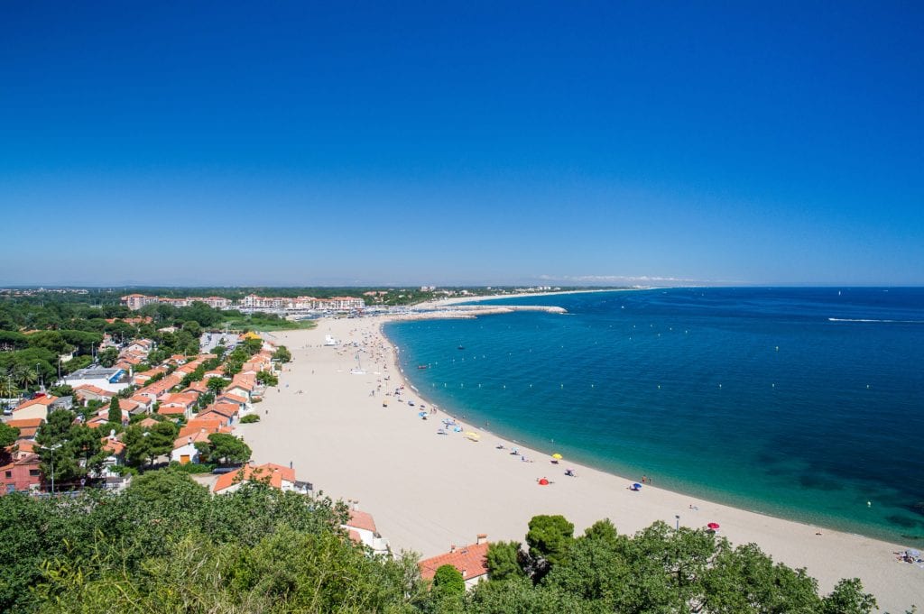 uitgestrekt zandstrand met daarachter bebossing en huizen in  Argelès-sur-Mer op een zonnige dag