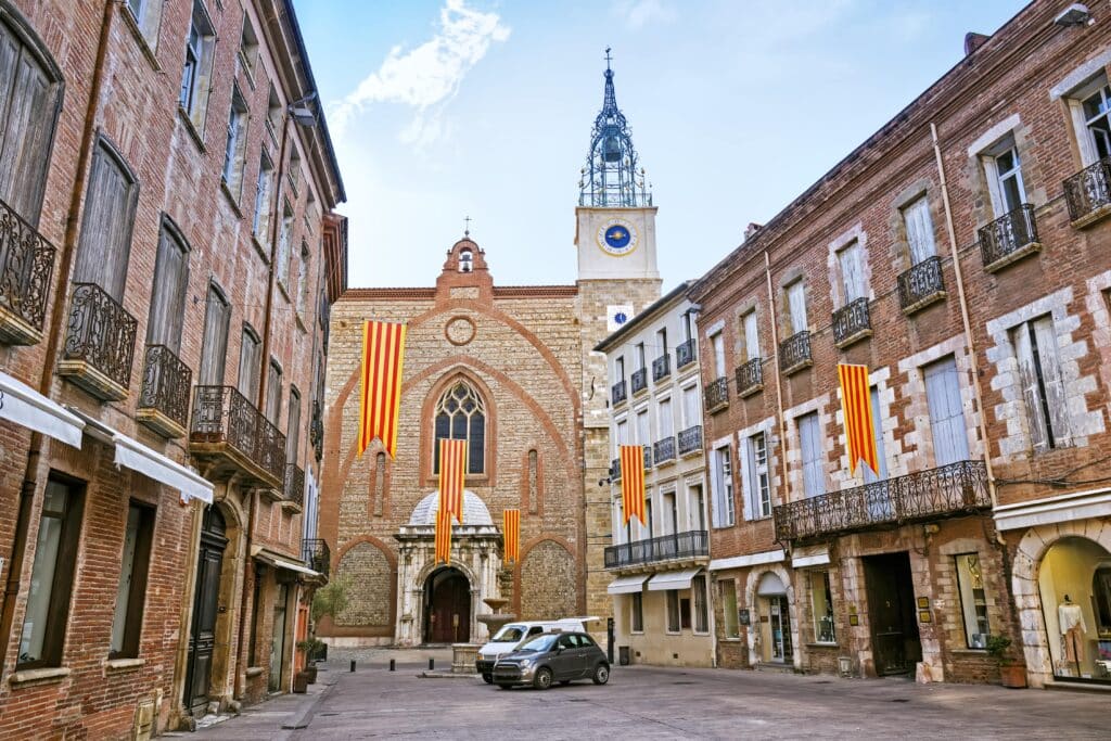 de Cathédrale Saint-Jean-Baptiste gelegen aan het eind van een straatje met twee auto's in Perpignan