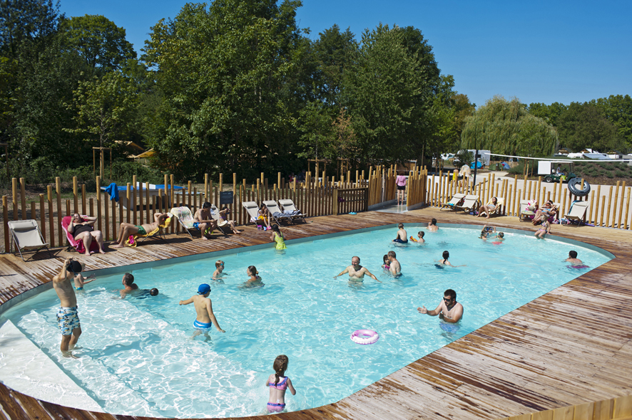 zwembad waarin kinderen en volwassenen zwemmen op Camping de Strasbourg. Het zwembad wordt omringd door een houten vlonder met een aantal ligstoelen