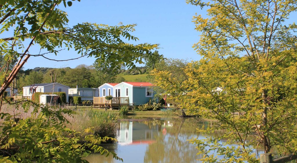 gekleurde stacaravans (lichtrgroen en lichtblauw) gelegen aan een vijver op Camping Le Marqueval