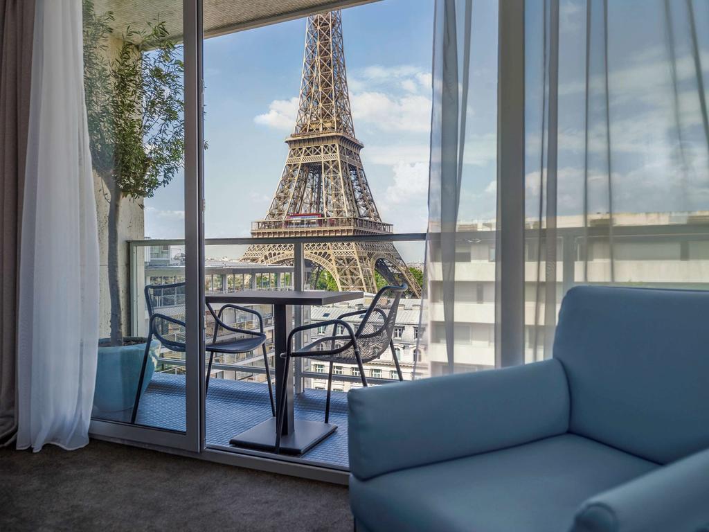 uitzicht op de Eiffeltoren gezien vanuit een hotelkamer van Hotel Pullman Paris met op de voorgrond een loungestoel en daarachter een terras met tafeltje en twee stoelen