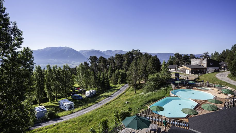 foto van het zwembad en een aantal campers en caravans tegen een berghelling op Camping Huttopia Font-Romeu