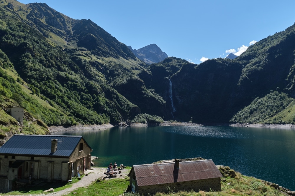 lac d'oô, meer omgeven door groene bergen en twee huisjes op de voorgrond