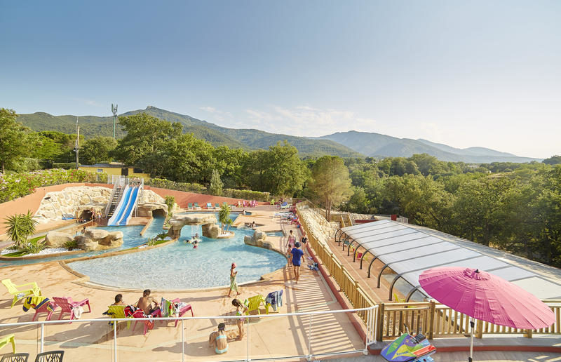 zwembad met twee glijbanen, waar enkele mensen rondlopen en kinderen in het water spelen, op Camping Les Albères in de Languedo-Roussillon