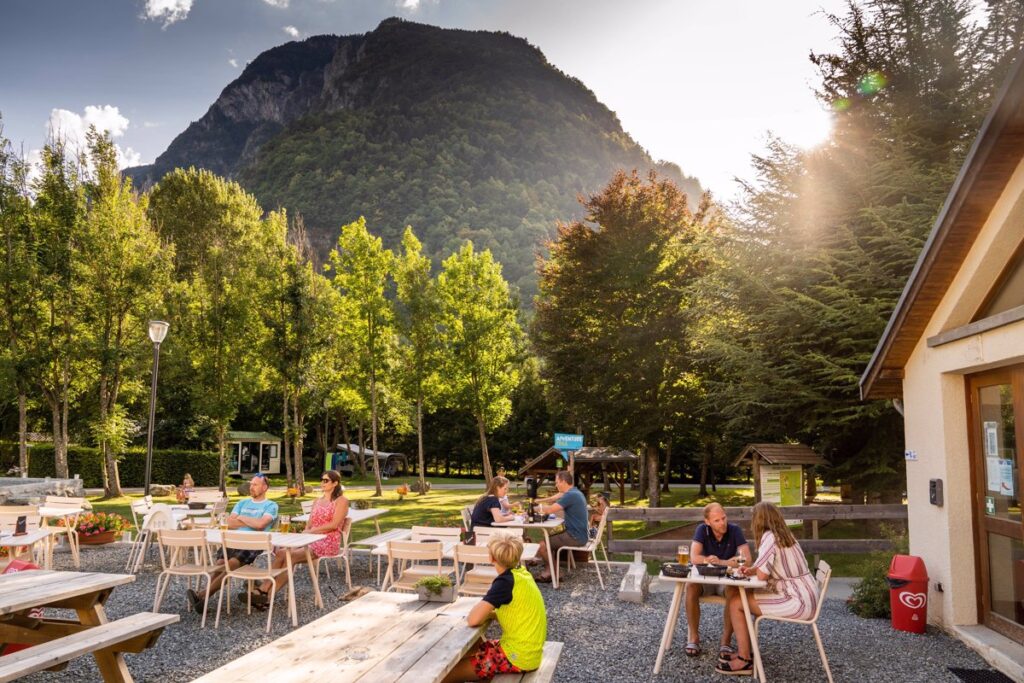 mensen die op het terras van camping RCN Belledonne zitten. Het terras wordt omringd door bergen en bomen.