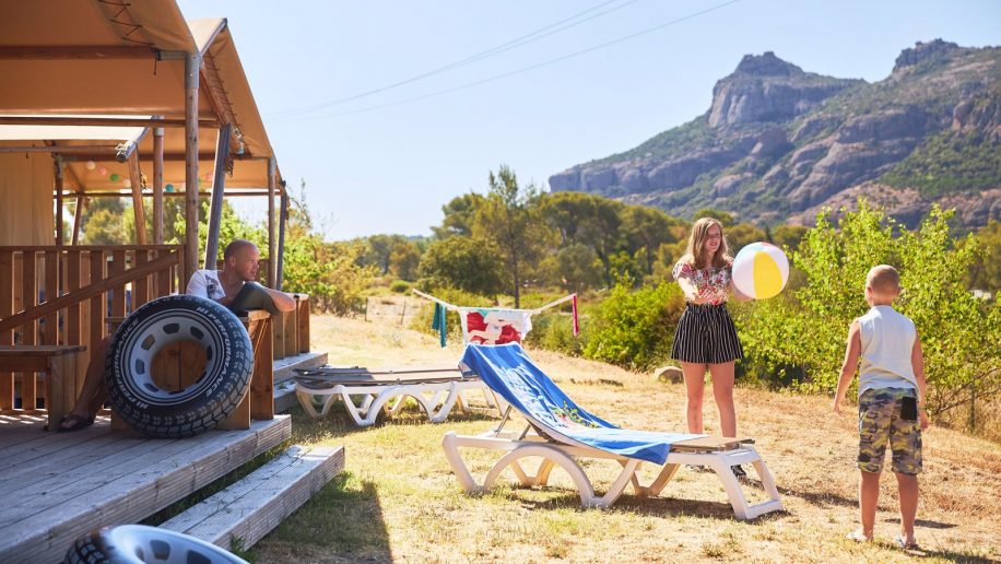 Een moeder die een strandbal naar haar zoontje gooit en een vader die vanaf het terras van de safaritent toekijkt.