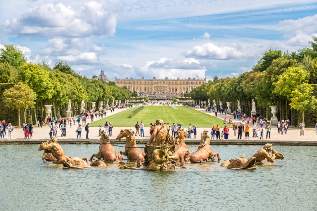 standbeeld in een fonteint met daarachter een druk park en helemaal achterin het paleis van Versailles