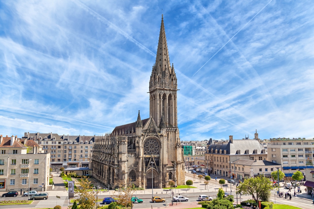 De kerk van Caen midden in de stad met daarom heen straten, huizen, bomen en auto's.