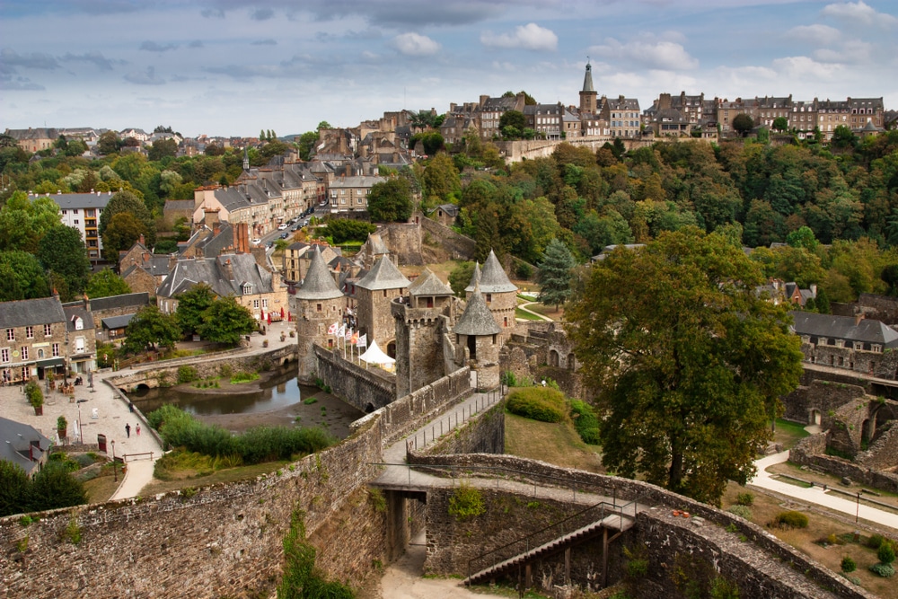Foto van de stad Fougères met een stenen omwalling, torens, middeleeuwse huizen en veel bomen.