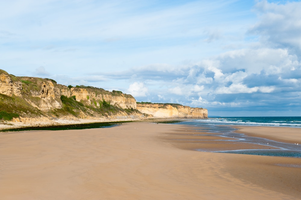 Het brede strand van Omaha Beach met krijtrotsen en zee.